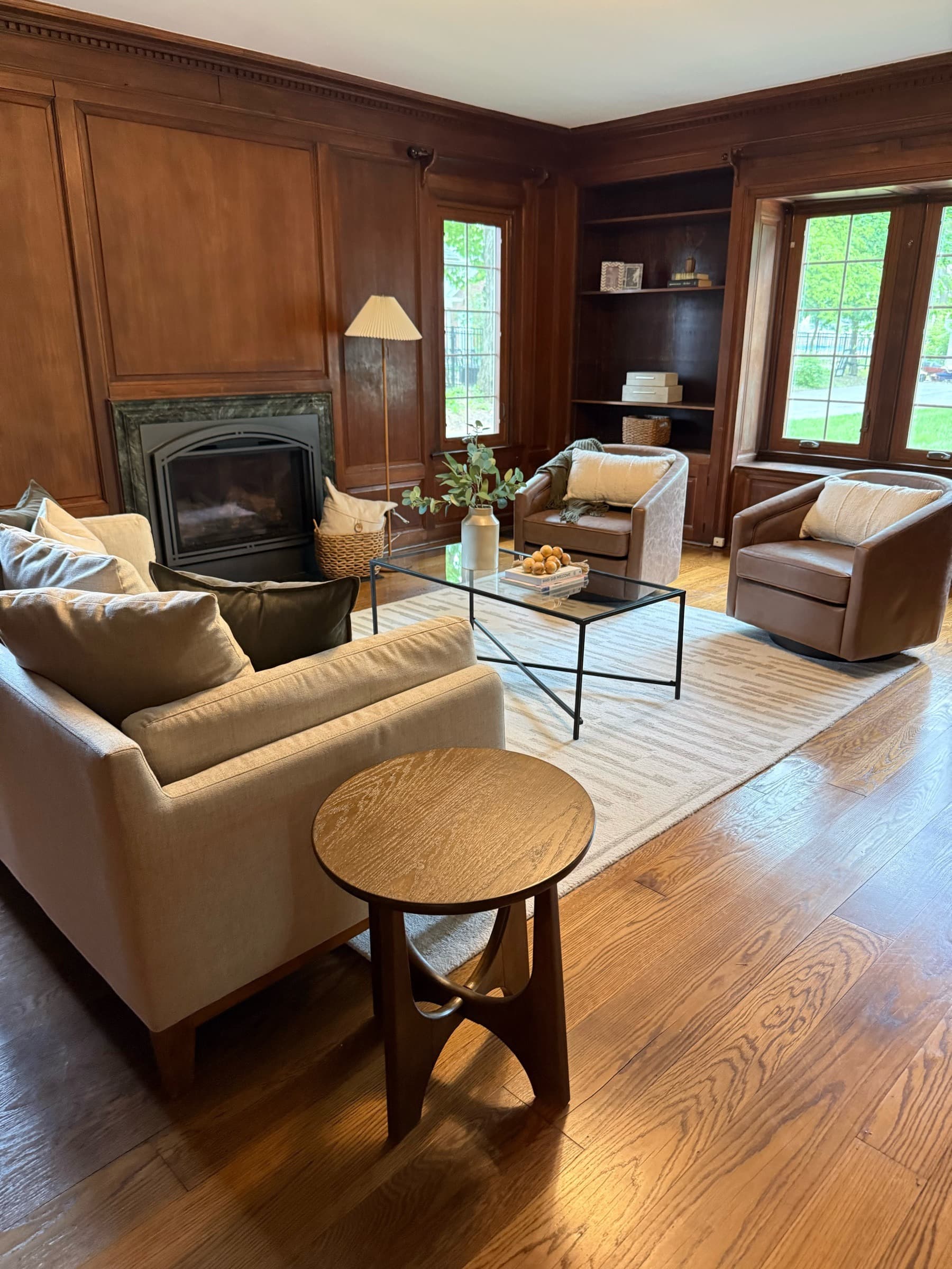 Wood-paneled den styled with warm neutral seating and a round side table